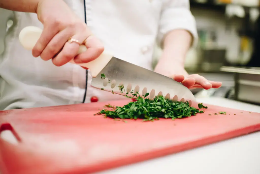 Chef chopping fresh parsley on red cutting board with knife