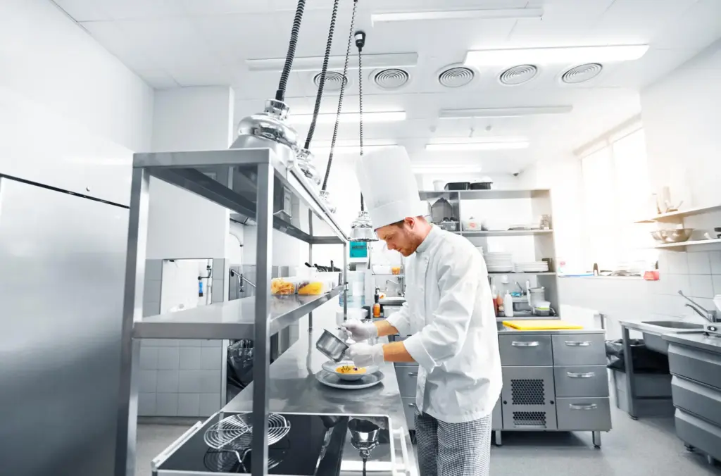 Chef in white uniform plating food in commercial kitchen