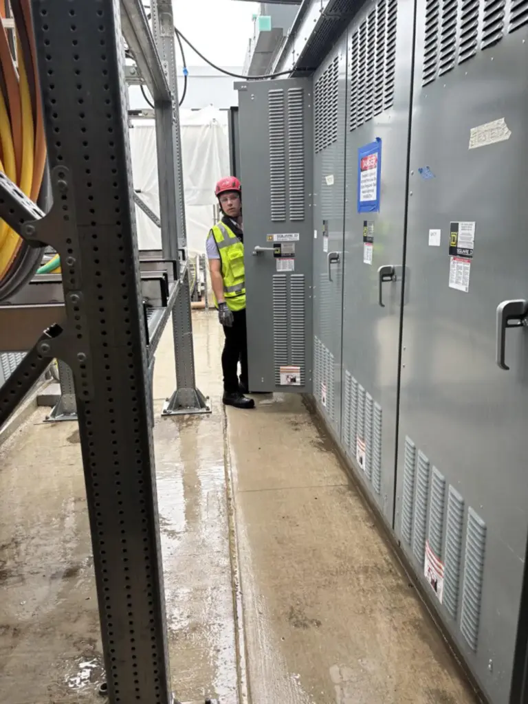 Electrical technician in safety gear inspecting a large power distribution cabinet