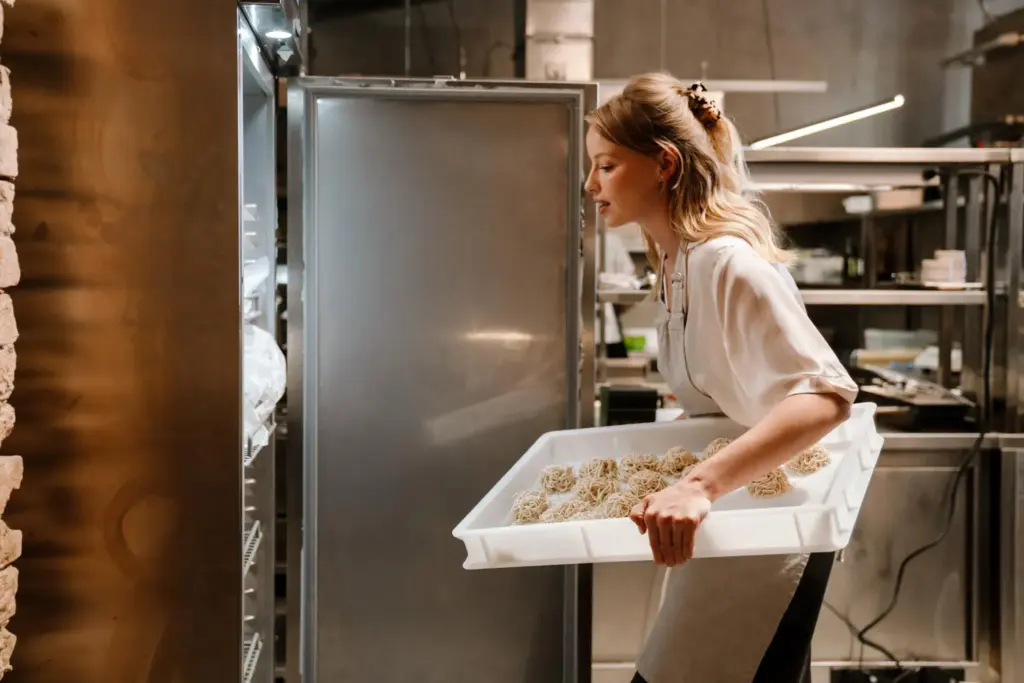 Female chef placing tray of fresh pasta into commercial refrigerator