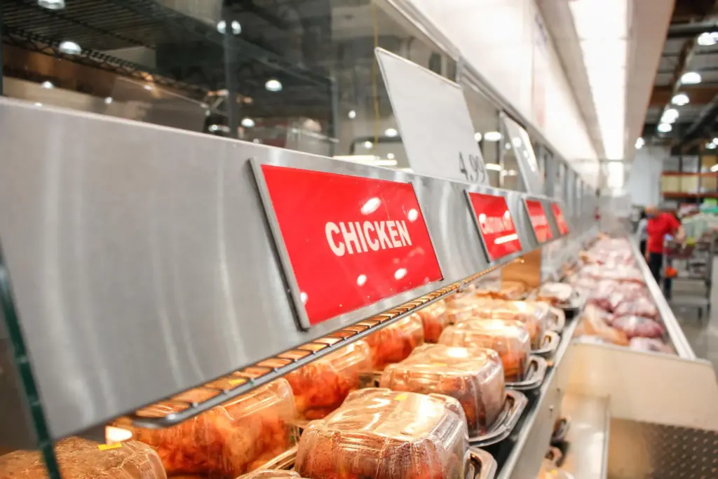 Rotisserie chickens in plastic containers under a red chicken sign