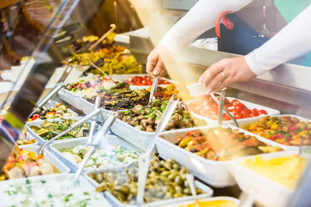 Server dishing fresh Mediterranean appetizers from a deli display case
